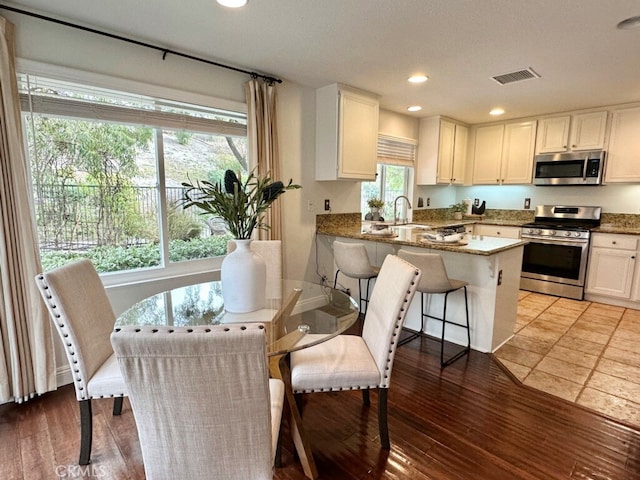 kitchen with stainless steel appliances, white cabinets, a kitchen bar, and light hardwood / wood-style flooring