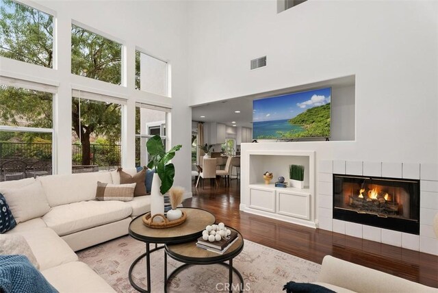 living room with a high ceiling, a tile fireplace, and wood-type flooring