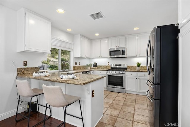 kitchen with a kitchen bar, kitchen peninsula, white cabinets, and appliances with stainless steel finishes