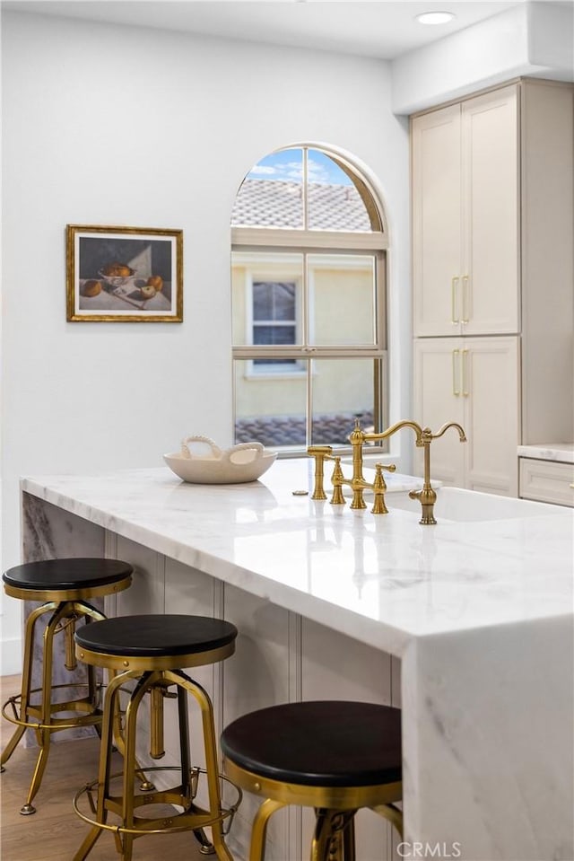 interior space with hardwood / wood-style flooring, light stone countertops, sink, and a kitchen bar