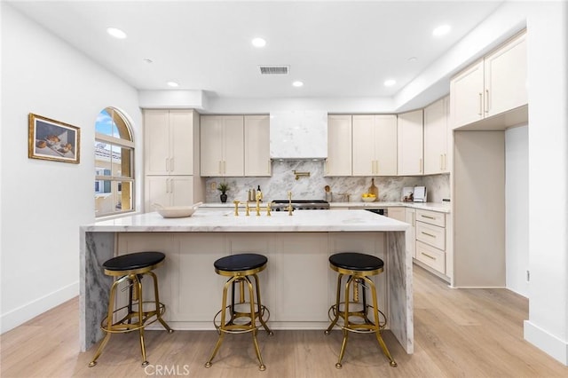 kitchen with light wood-type flooring, a kitchen island with sink, a kitchen bar, and decorative backsplash