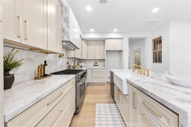 kitchen with custom range hood, high end stainless steel range, light stone counters, and light hardwood / wood-style floors