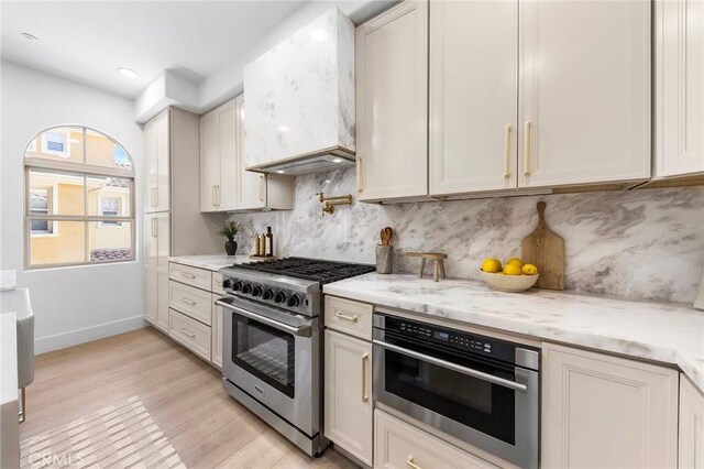 kitchen with light stone counters, white cabinetry, light wood-type flooring, appliances with stainless steel finishes, and decorative backsplash