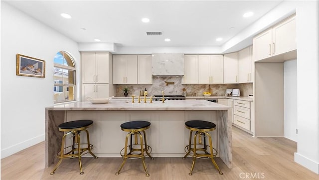 kitchen featuring a breakfast bar area, white cabinets, decorative backsplash, light hardwood / wood-style floors, and a center island with sink