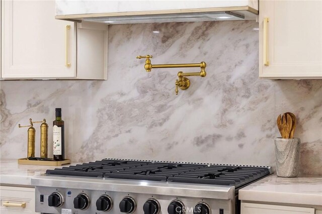 room details with tasteful backsplash, stainless steel gas range oven, light stone countertops, and white cabinets