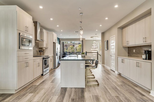 kitchen featuring pendant lighting, a center island with sink, stainless steel appliances, a kitchen bar, and wall chimney exhaust hood