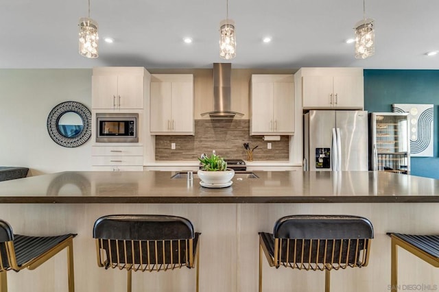 kitchen featuring appliances with stainless steel finishes, wall chimney range hood, and decorative light fixtures