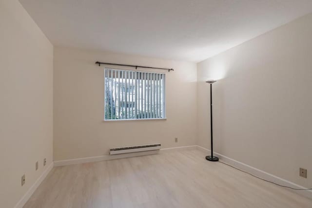 spare room featuring baseboard heating and light hardwood / wood-style flooring