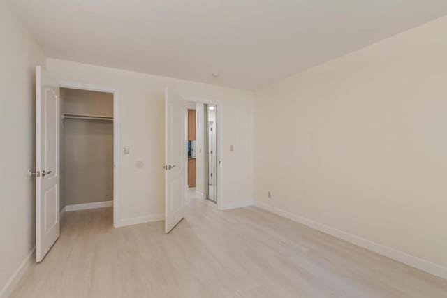 unfurnished bedroom with a closet, a spacious closet, and light hardwood / wood-style flooring