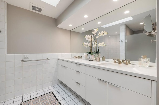 bathroom featuring tile patterned flooring, vanity, tile walls, and a skylight