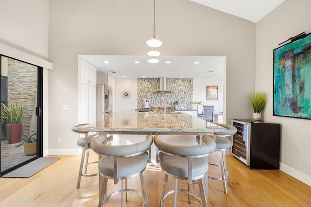 kitchen featuring hanging light fixtures, backsplash, stainless steel refrigerator with ice dispenser, white cabinets, and wall chimney exhaust hood