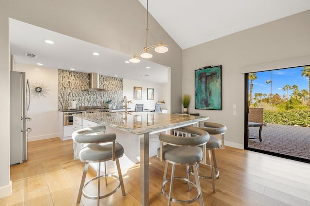 kitchen featuring hanging light fixtures, a kitchen breakfast bar, stainless steel appliances, light stone countertops, and wall chimney range hood