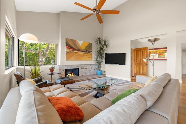 living room featuring ceiling fan, a towering ceiling, a fireplace, and light hardwood / wood-style floors