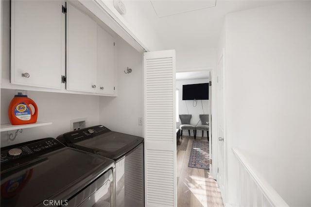 clothes washing area with independent washer and dryer, hardwood / wood-style floors, and cabinets