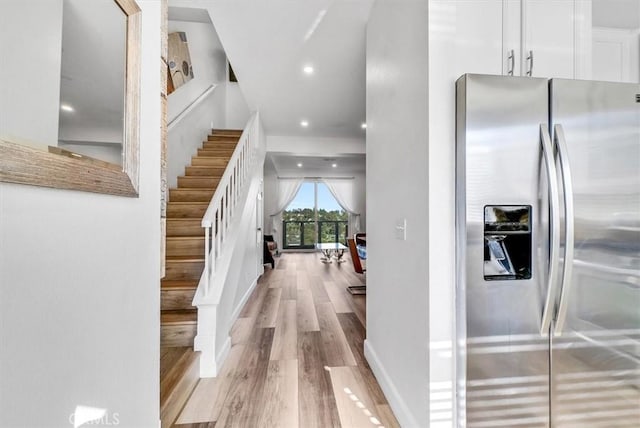 interior space featuring light wood-type flooring, stainless steel fridge with ice dispenser, and white cabinets