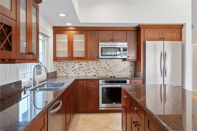 kitchen with sink, dark stone countertops, stainless steel appliances, light tile patterned flooring, and decorative backsplash