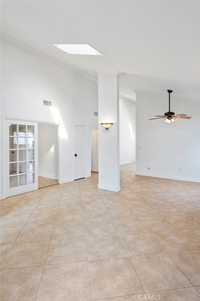 empty room featuring ornamental molding, light tile patterned flooring, ceiling fan, and a skylight