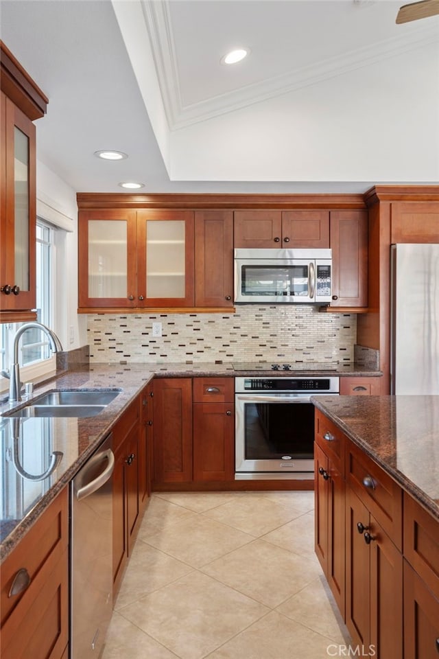 kitchen featuring sink, ornamental molding, appliances with stainless steel finishes, dark stone counters, and decorative backsplash