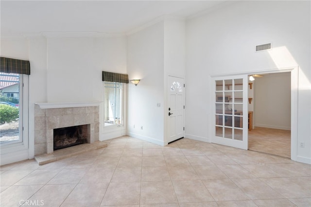 unfurnished living room with a tiled fireplace, ornamental molding, a high ceiling, light tile patterned floors, and ceiling fan