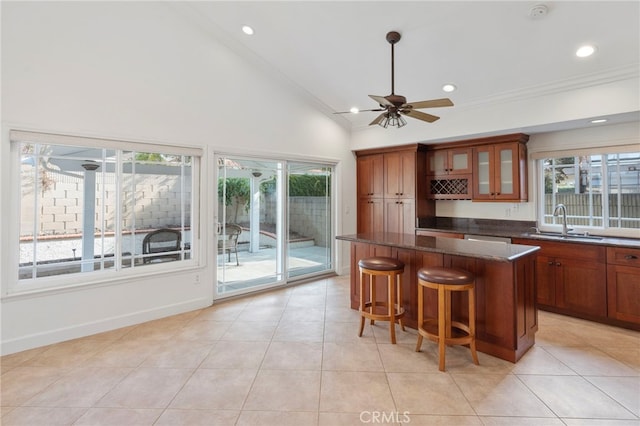 kitchen featuring sink, light tile patterned floors, a kitchen breakfast bar, a kitchen island, and dark stone counters