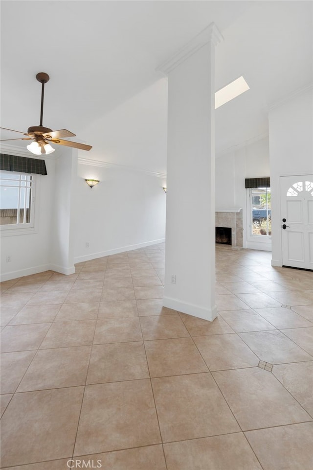 spare room with high vaulted ceiling, a fireplace, ornamental molding, light tile patterned floors, and ceiling fan