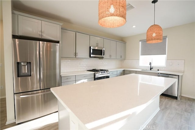 kitchen with sink, appliances with stainless steel finishes, hanging light fixtures, tasteful backsplash, and a kitchen island