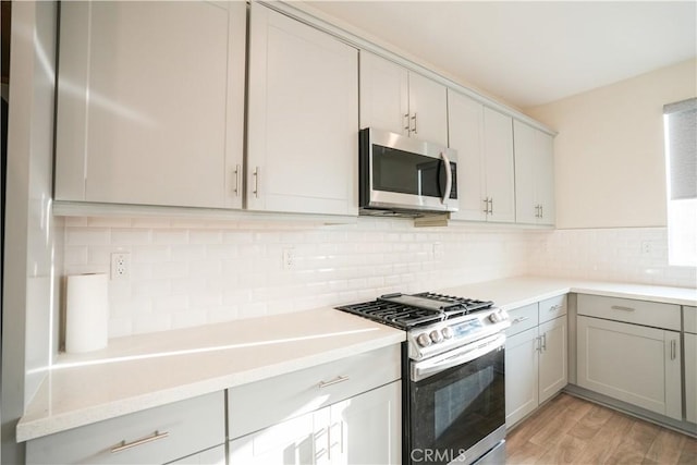 kitchen with tasteful backsplash, appliances with stainless steel finishes, gray cabinets, and light wood-type flooring