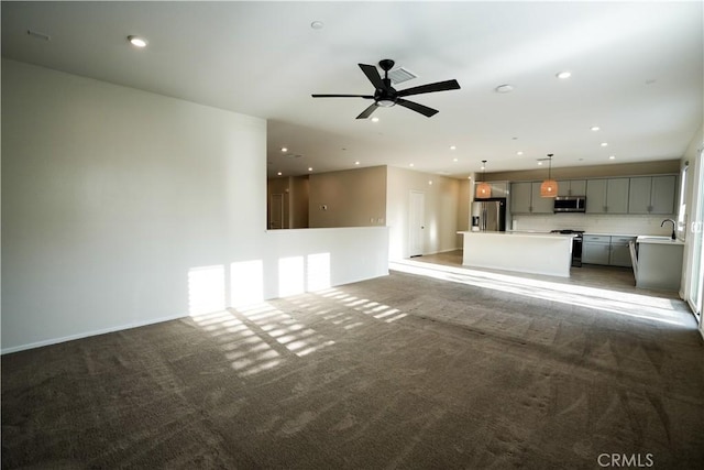 unfurnished living room with dark carpet, ceiling fan, and sink