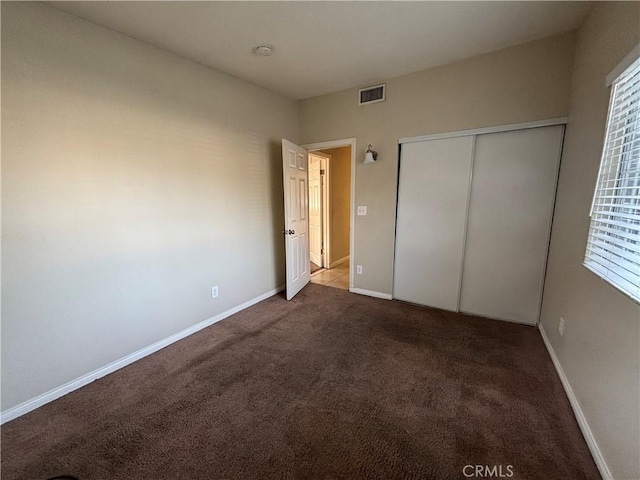 unfurnished bedroom with dark carpet and a closet