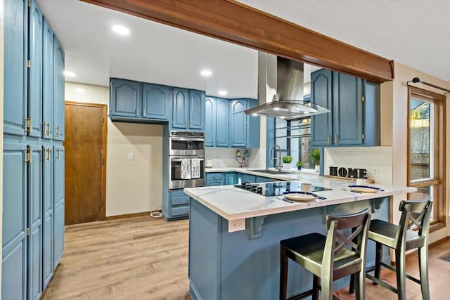 kitchen featuring extractor fan, a kitchen breakfast bar, kitchen peninsula, blue cabinetry, and light hardwood / wood-style flooring