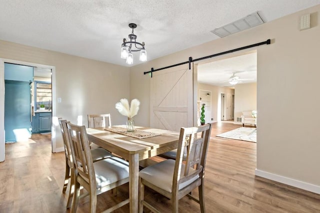 dining space with a barn door, a textured ceiling, and light wood-type flooring