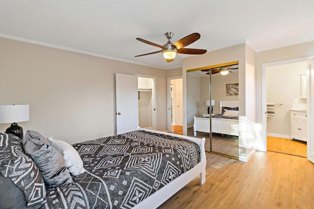 bedroom featuring hardwood / wood-style floors, ceiling fan, crown molding, ensuite bath, and a closet