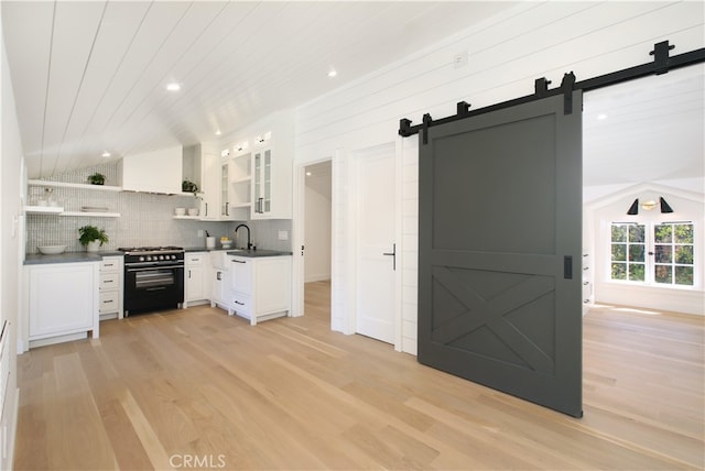 kitchen featuring a barn door, range with gas stovetop, vaulted ceiling, tasteful backsplash, and white cabinets