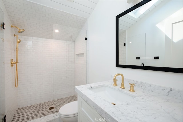 bathroom with vanity, vaulted ceiling, tiled shower, and toilet