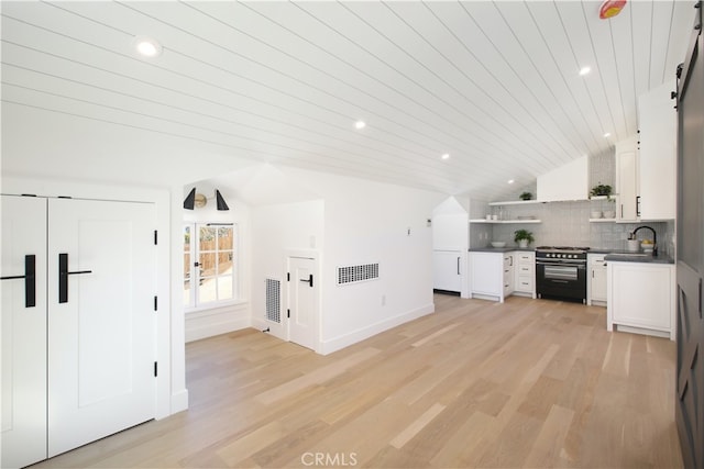 interior space with vaulted ceiling, sink, high end range, white cabinets, and decorative backsplash