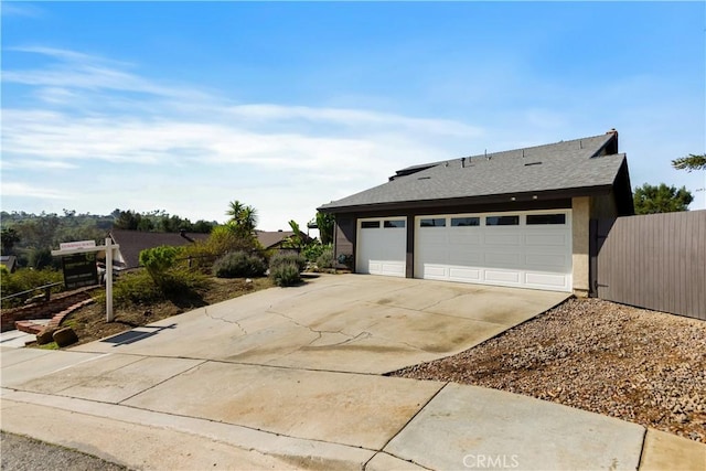 view of front of house with concrete driveway, fence, a garage, and roof with shingles