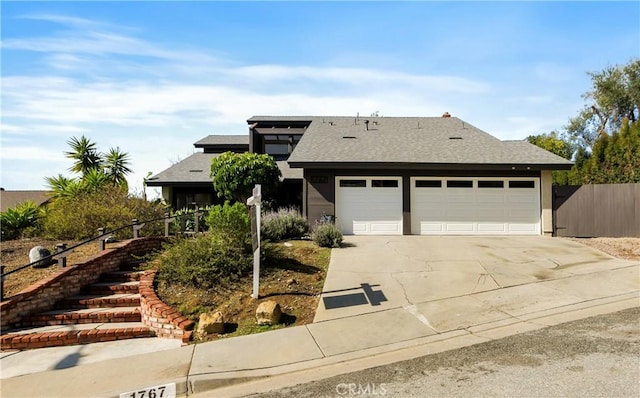 view of front of home with fence, concrete driveway, a shingled roof, a garage, and stairs