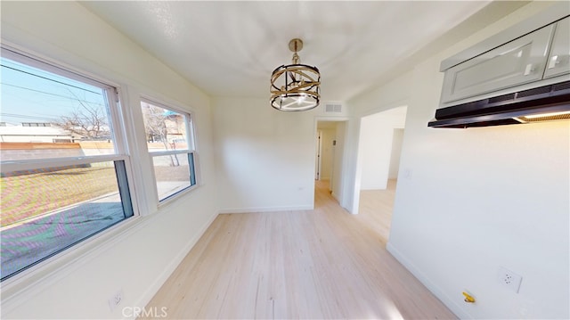 unfurnished dining area with a chandelier and light hardwood / wood-style flooring