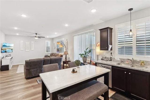 kitchen featuring dark brown cabinetry, sink, light wood-type flooring, stainless steel dishwasher, and pendant lighting