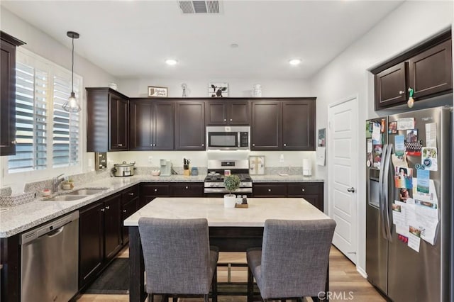 kitchen featuring stainless steel appliances, decorative light fixtures, a center island, and sink