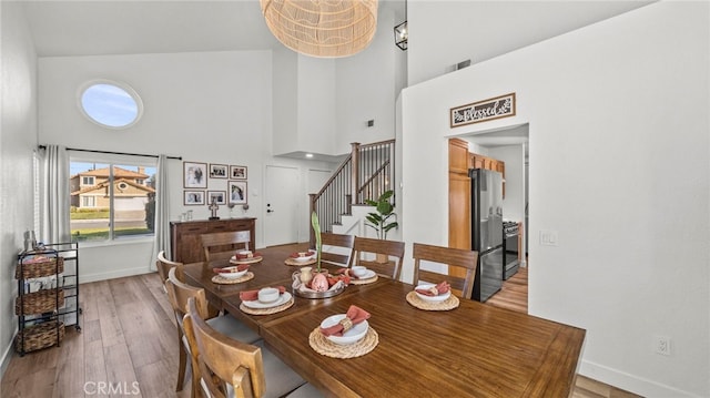 dining room featuring light wood-type flooring, a high ceiling, baseboards, and stairs