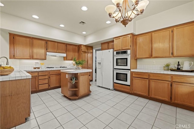 kitchen featuring white appliances, tile counters, a kitchen island, decorative light fixtures, and a chandelier