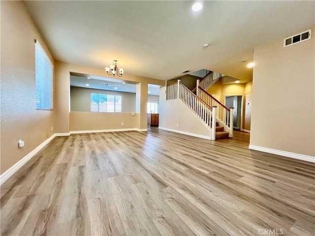 unfurnished living room with an inviting chandelier and light hardwood / wood-style flooring