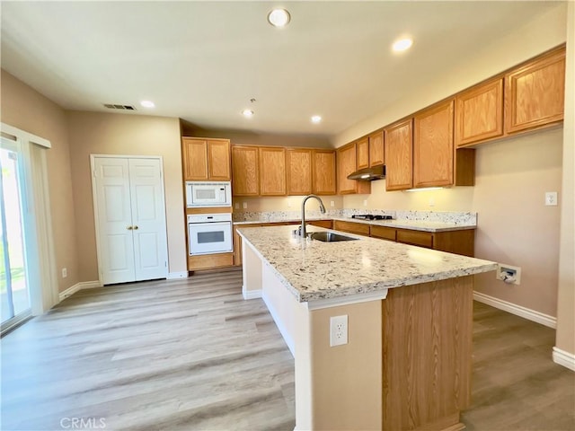 kitchen featuring sink, white appliances, light hardwood / wood-style flooring, a kitchen island with sink, and light stone countertops