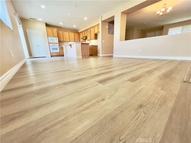 unfurnished living room featuring an inviting chandelier, light hardwood / wood-style flooring, and a wealth of natural light