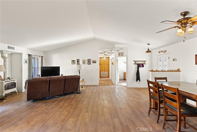 living room with a wood stove, visible vents, vaulted ceiling, and wood finished floors