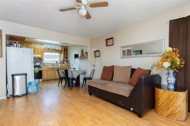 living room with ceiling fan, sink, a textured ceiling, and light wood-type flooring