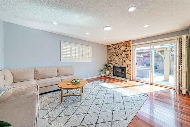 living room featuring a stone fireplace, light hardwood / wood-style floors, and a textured ceiling