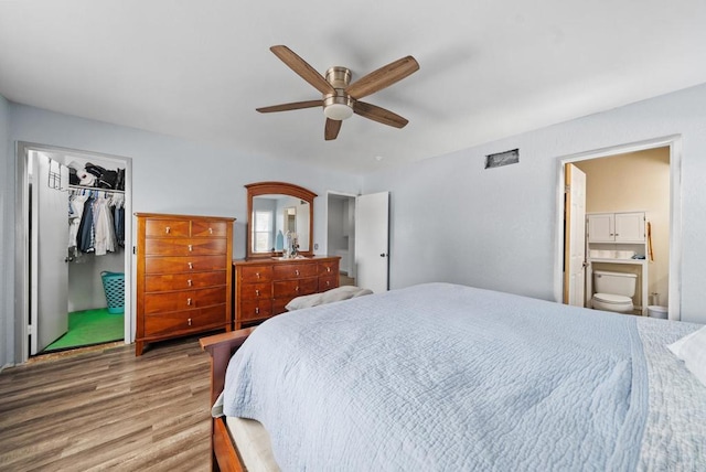 bedroom with ceiling fan, ensuite bathroom, wood-type flooring, a walk in closet, and a closet