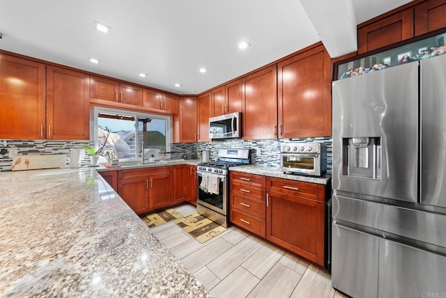 kitchen featuring tasteful backsplash, light stone countertops, appliances with stainless steel finishes, and sink